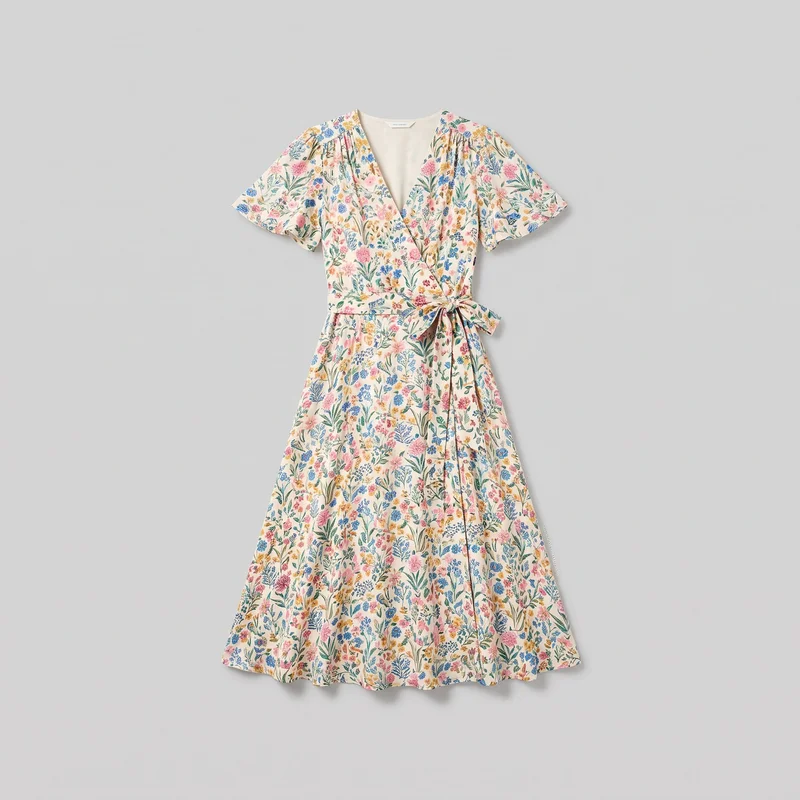 A mostly complete front view shows a women's floral print wrap midi dress displayed as a standalone garment. It has a surplice V neckline, short flutter sleeves with gathered shoulder and yoke details, a defined waist seam, and an integrated side self-tie sash. The wrap front and skirt overlap continue into an A-line silhouette with a softly flared hem.