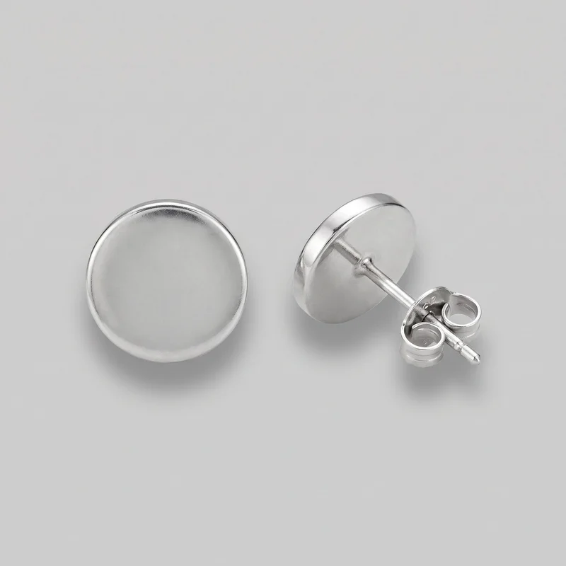 A pair of silver round disc stud earrings is shown as a standalone product. One earring faces forward, displaying its smooth, slightly domed circular face and thick raised rounded rim, while the other is angled to show its straight post and butterfly clutch backing. No logos, stones, engraving, or additional embellishments are visible.