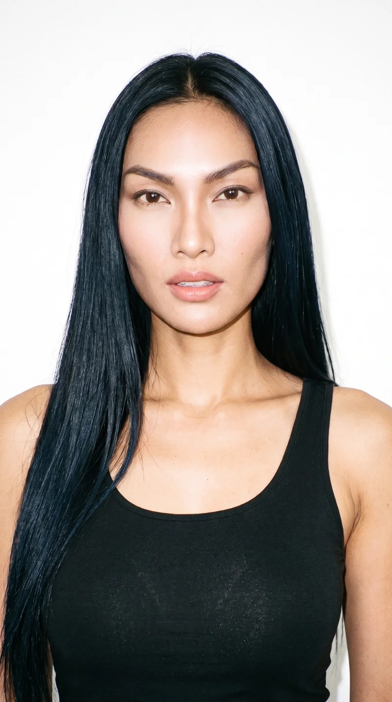 This 32-year-old woman has a Southeast Asian appearance and a medium skin tone with a neutral undertone. Her diamond-shaped face has a narrow forehead and jaw, with the greatest width at the cheekbones. She has thin eyebrows, very dark near-black eyes, and full lips. Her deep black hair falls long and straight without waves or layers.