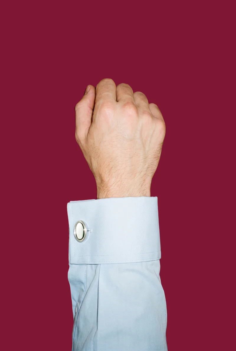A man's hand and wrist are shown from above with the knuckles facing forward, wearing silver classic cufflinks. The image uses a flat claret-colored backdrop.