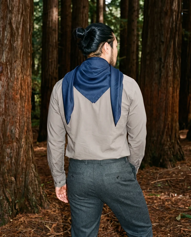 A 23-year-old Chinese male model wears a men’s navy silk scarf, shown from the back in a three-quarter-length frame with his hands behind his back. A redwood grove serves as the backdrop.