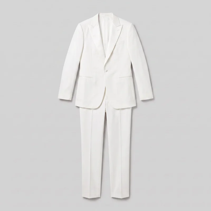 A white two-piece tailored dinner-jacket tuxedo is shown front-facing as a standalone product. The structured single-breasted blazer has notched lapels, a visible one-button closure, long sleeves, a rounded hip-length hem, a welt chest pocket, horizontal lower welt pockets, and vertical front shaping seams. Most of the coordinating full-length straight-leg trousers are visible beneath the blazer, with straight hems and pressed front creases.