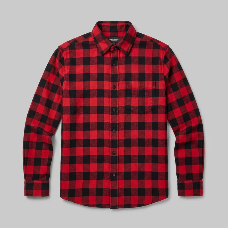 A red buffalo check flannel shirt is shown laid flat in a mostly complete front view. The long-sleeve button-up shirt has a pointed button-down collar, full front button placket, shoulder yoke, two chest patch pockets with rectangular flap seams, button cuffs, and a curved shirt-tail hem.