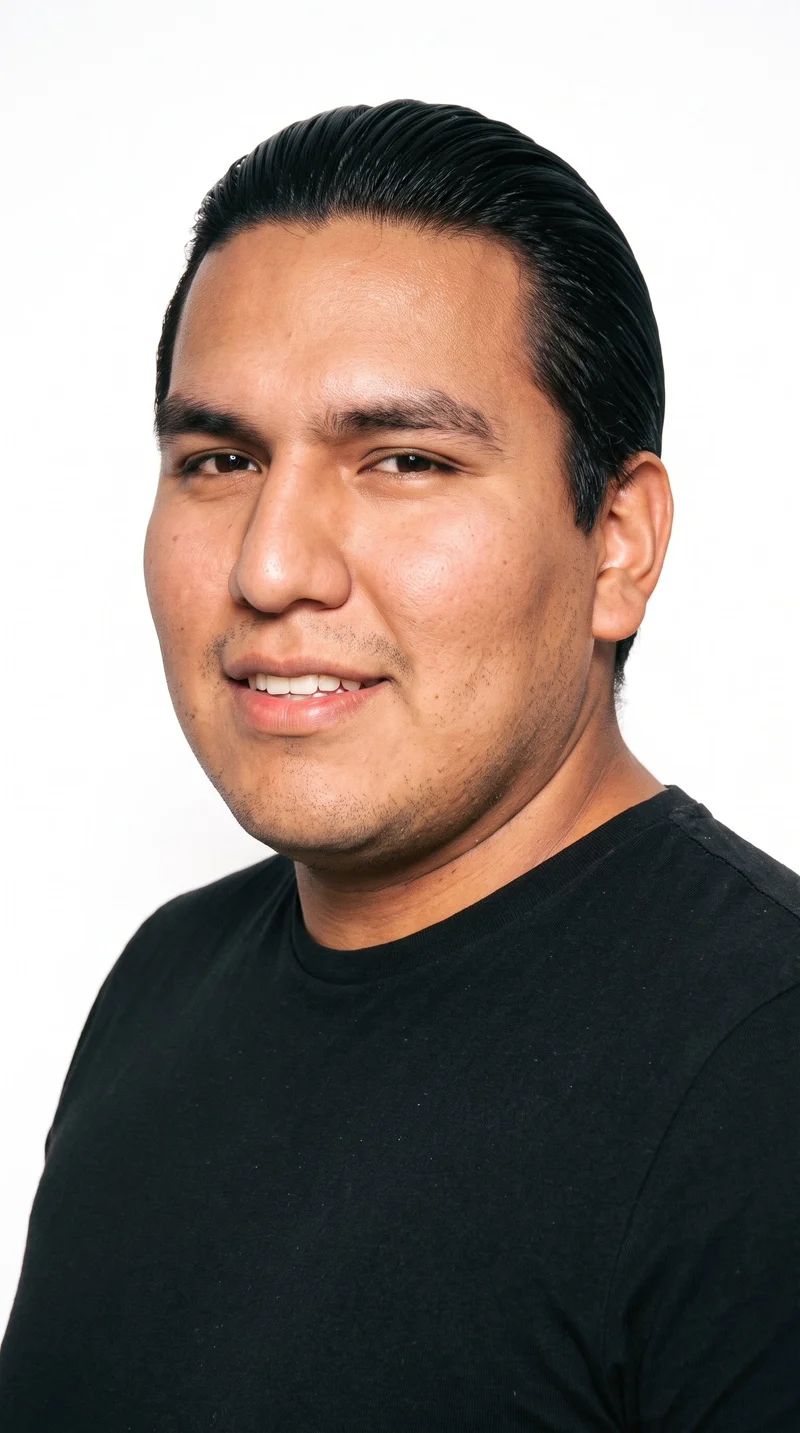 An 18-year-old Indigenous American man with brown skin, a warm golden sheen, and a red-copper undertone. His face has a Roman structure, with strong classical features, a prominent nose line, and a defined jaw. He has thick eyebrows, very dark near-black eyes, and full lips. His deep black hair is combed flat and back close to the head, and dense stubble forms a dark, defined layer across the beard area.