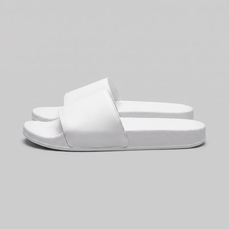 A pair of white slip-on slide sandals is shown in side profile, with one sandal overlapping the other. Each sandal has a flat low-platform sole, a rounded open toe, an open back, and a single wide band crossing the forefoot. The raised footbed rim, perimeter stitching on the band, and pebbled sole sidewalls with a thin lower edge line are visible.