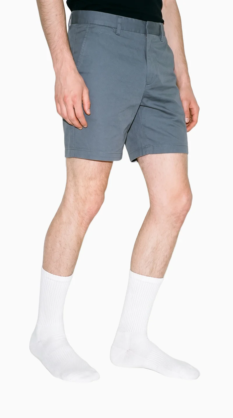 A man's lower legs are shown from a front three-quarter angle with the knees turned inward, wearing white cushioned sports socks. The image uses a flat seasalt-colored backdrop.