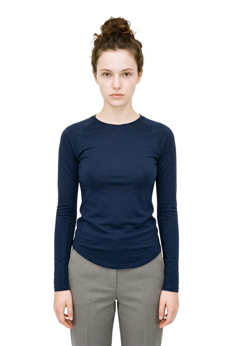 An 18-year-old Caucasian female model wears a navy long-sleeve base layer in an upper-body front view. Her shoulders are dropped, and the garment is shown against a pure white backdrop.
