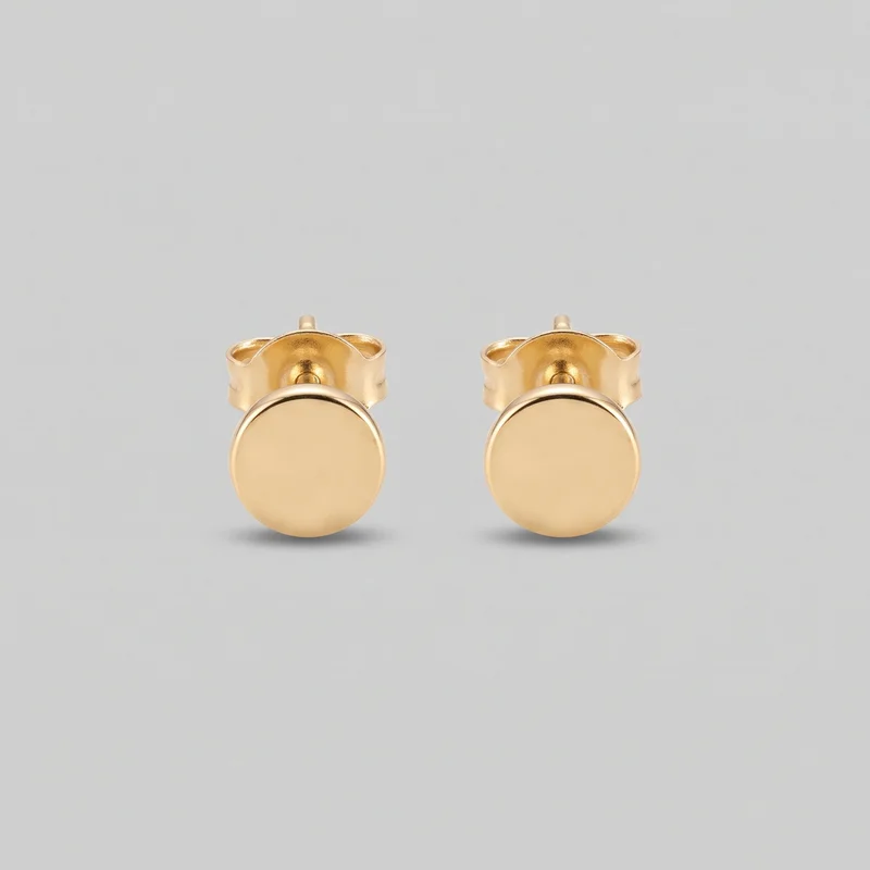 A pair of round gold stud earrings is shown as standalone jewelry. Each earring has a smooth circular front plate with a softly rounded rim, a straight post, and a butterfly clutch backing visible behind the disc; the plain symmetrical design has no visible stones, engraving, logos, or other embellishment.