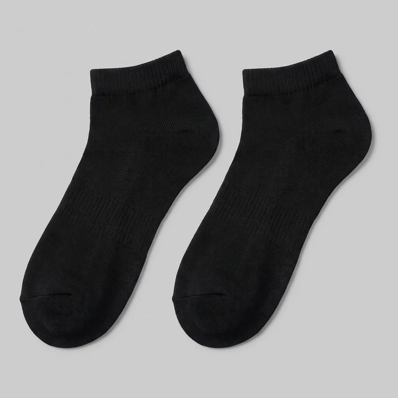 A complete pair of black low-cut ankle socks is laid flat and viewed from above. The socks have short ribbed cuffs, fine vertical knit ribs, shaped heel pouches, rounded toes, and visible toe seams, with no logos or embellishments.
