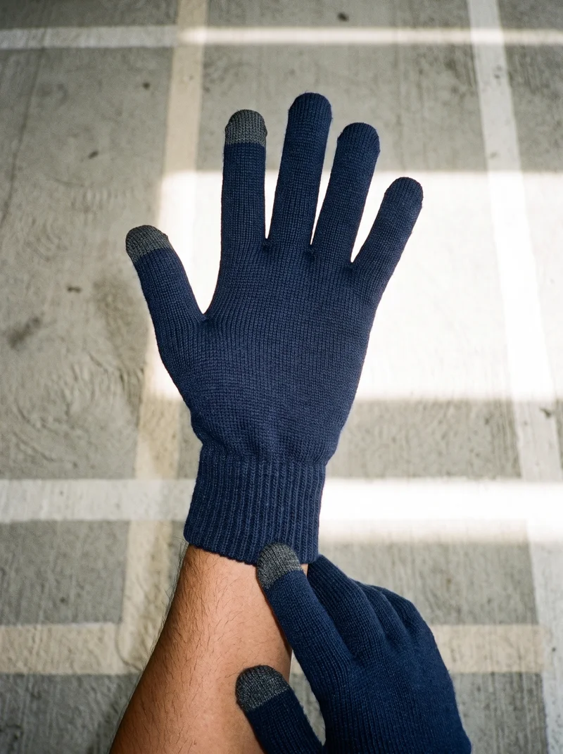 A hand wearing men's navy touchscreen gloves is shown from above, with one gloved hand touching the wrist area. The concrete parking garage serves as the backdrop.