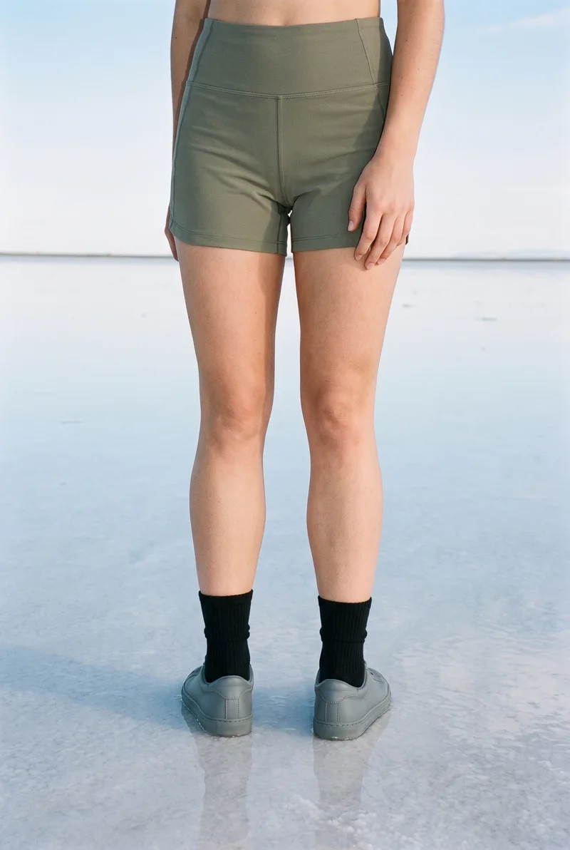 Women's black crew socks shown on a female model's lower body in a front view, with the model standing on tiptoes. A salt flats reflection serves as the backdrop.