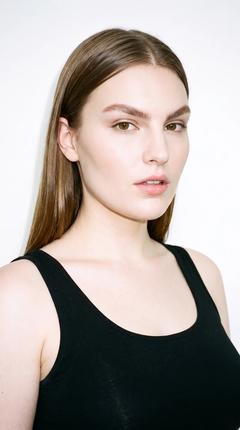 A 25-year-old Caucasian woman with porcelain skin and a cool undertone. Her diamond-shaped face has a narrow forehead and jaw, with the greatest width at the cheekbones. She has thin eyebrows, brown eyes, and medium-sized lips. Her light-brown hair is straight, smooth, and parted evenly at the centre.