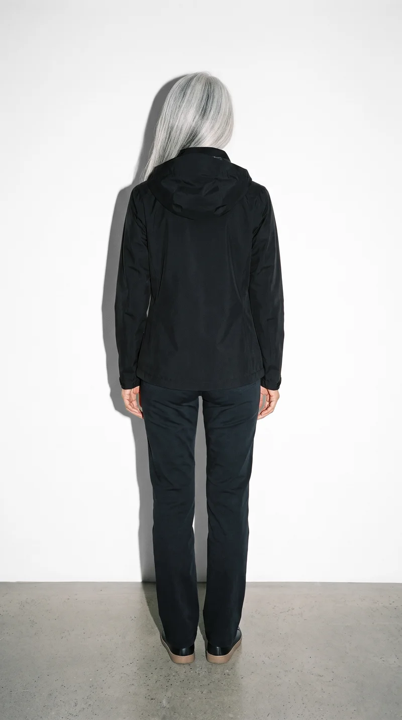 A 54-year-old Chinese woman wears a women's black hardshell jacket in a full-body back view. She stands in a relaxed pose against a Seasalt studio-wall backdrop.