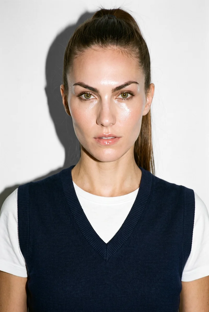 A 28-year-old Caucasian woman wears a women's navy knit sweater vest in a bust-length front view. Her head is level and her confident expression is visible against a pure white studio-wall backdrop.