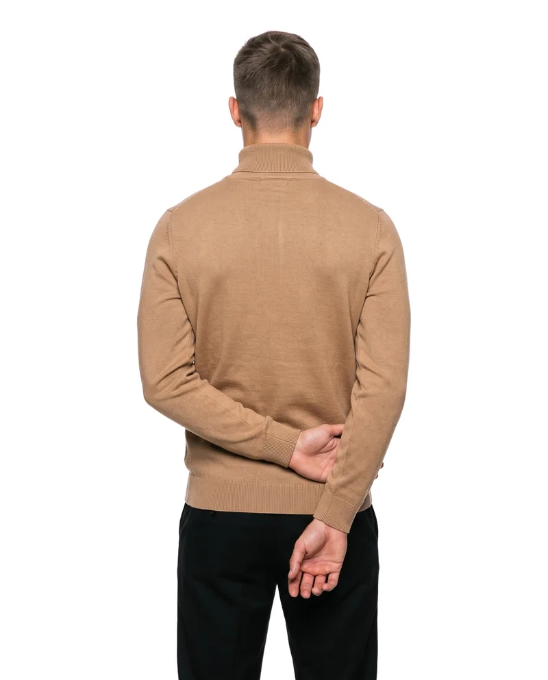 A 20-year-old Caucasian male model wears a men's camel roll-neck, shown in a three-quarter-length rear view with his hands behind his back. The garment is presented against a pure white backdrop.