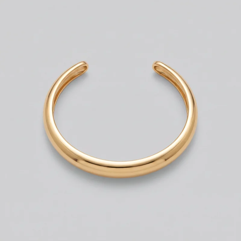 A standalone close view shows a women's gold cuff bracelet lying flat. The bracelet has a C-shaped open design with a visible gap between its blunt, rounded ends, a domed outer face, raised rounded edges, and a recessed inner channel near the opening. Its polished surface is smooth and free of stones, charms, logos, prints, or other embellishments.