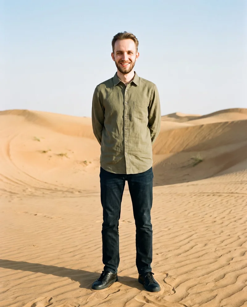 A 20-year-old Slavic male model wears an olive linen shirt in a full-body front view, standing with his hands behind his back and a natural expression. Death Valley dunes form the backdrop.