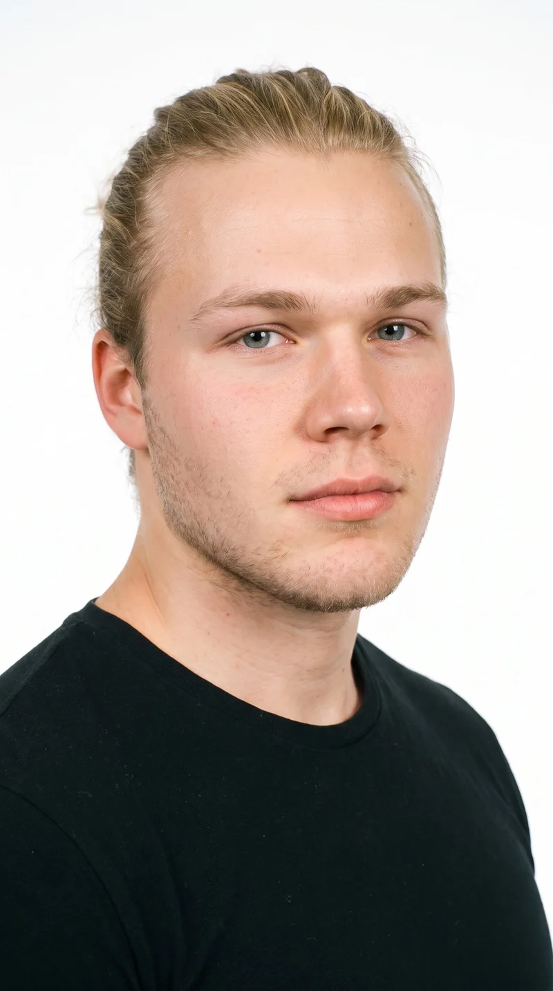 An 18-year-old Caucasian male with lightly tanned fair skin and a cool undertone. His face is round, with soft, full contours, gentle curves, and few angles. He has medium-thick eyebrows, blue eyes with a cool undertone, and full lips. His mid-tone blonde hair is longer and gathered into a knot at the back, with the sides drawn up. Fine, closely trimmed stubble lightly covers the beard area.