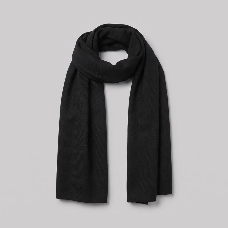 A rectangular black wool scarf is arranged in a loose loop at the upper section, with two straight ends hanging vertically. Its even-width panels have soft folded volume, squared plain-finished ends, and a subtle all-over diagonal herringbone weave texture.