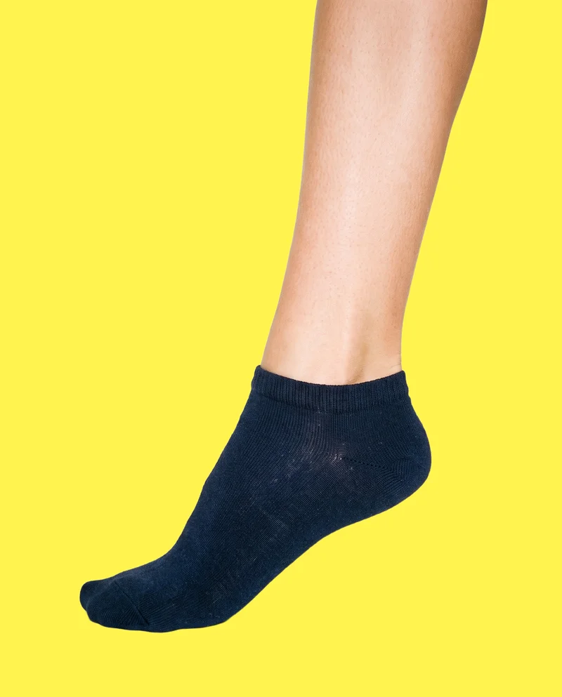 A navy ankle sock shown from the side with the toe pointed. The ankle-level framing isolates the sock against a flat lemon-yellow backdrop.