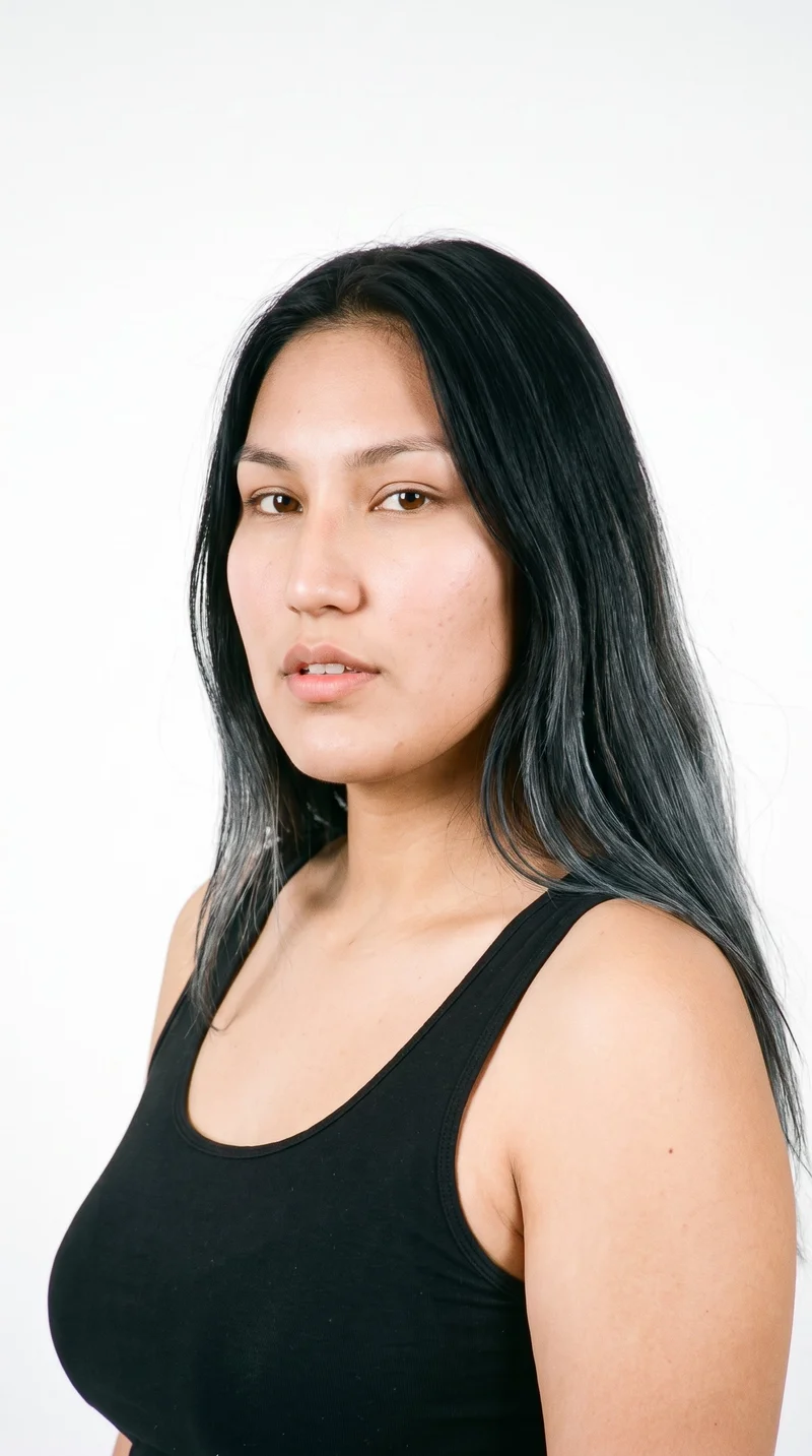 An 18-year-old Indigenous American woman with a medium, neutral-toned complexion has a long face that is more elongated than wide, with a tall forehead and elongated cheeks. Her eyebrows are medium in thickness, and she has brown eyes and medium-sized lips. Her deep black hair is long, worn loose past the shoulders with natural volume.