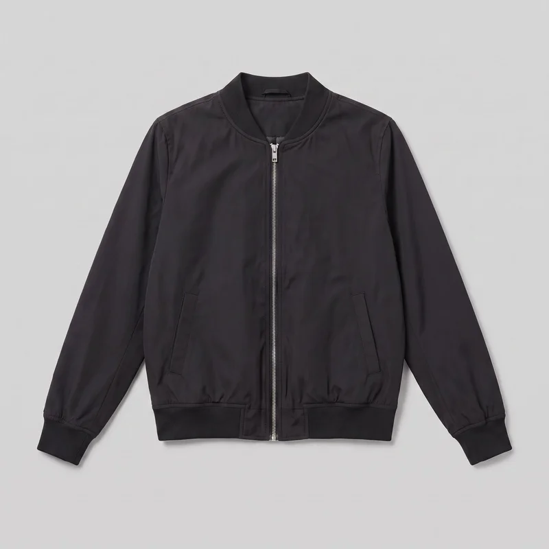 A black women's bomber jacket is shown laid flat in a standalone front view. The waist-length jacket has a straight blouson silhouette, a rounded ribbed collar, long set-in sleeves with ribbed cuffs, and a straight ribbed bottom hem. Its full-length center zipper, shoulder and armhole panel seams, subtle gathering at the ribbed trim, and two lower angled welt pockets are visible.