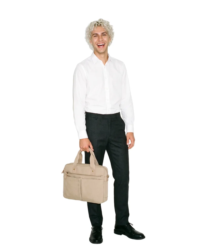 A 19-year-old Caucasian man is shown full body from a front three-quarter angle, laughing with a men's beige canvas crossbody bag positioned at his side. The image uses a pure white flat-color backdrop.