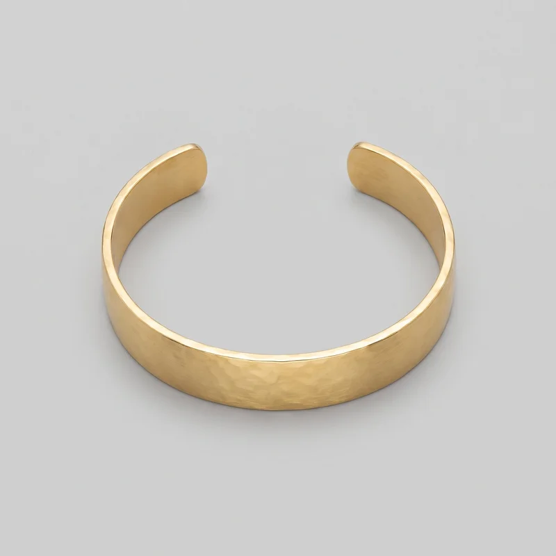 A standalone angled view shows a wide gold open cuff bracelet with a smooth curved band, a visible gap, and squared rounded terminals. Its brushed central face is bordered by raised polished rims, with softly beveled ends and a slightly concave interior. No logos, stones, charms, engravings, or other embellishments are visible.