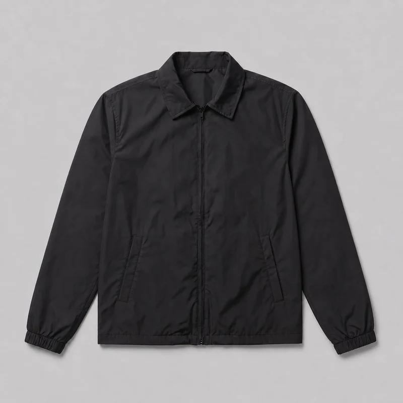A men's black windbreaker is shown laid flat in a mostly complete front view. The regular-fit jacket has a pointed spread collar, centered full-length zipper, long sleeves with gathered elastic cuffs, two angled lower-front welt pockets, visible shoulder seams, and a straight hem.
