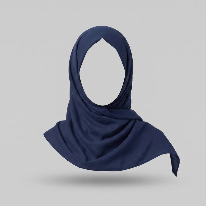 A navy cotton hijab is arranged on a head form in a front-facing draped wrap. It has an open oval face area, a smooth crown, a neatly folded edge around the opening, layered side panels, and soft gathers around the neck. The loose end extends across the front and over one shoulder, with narrow cleanly finished edges.