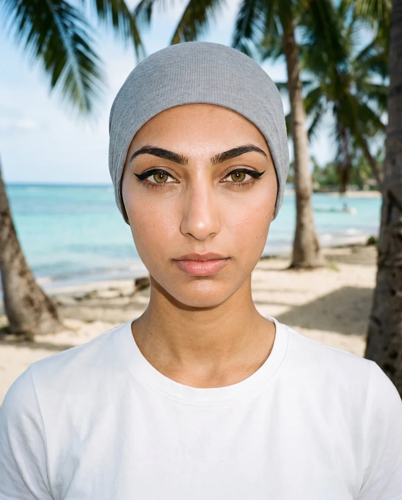 A 19-year-old Arab woman wears a grey underscarf in a front-facing bust composition with her head level. The Palm Tree Beach setting appears as the backdrop.