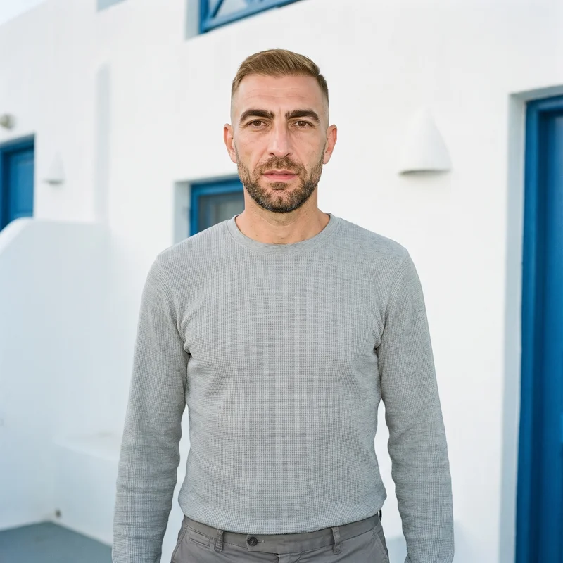 A 51-year-old Caucasian man wears a men's grey waffle-knit long-sleeve tee in an upper-body, front-facing view. His arms are relaxed, and a Greek Villa White Blue backdrop is visible behind him.