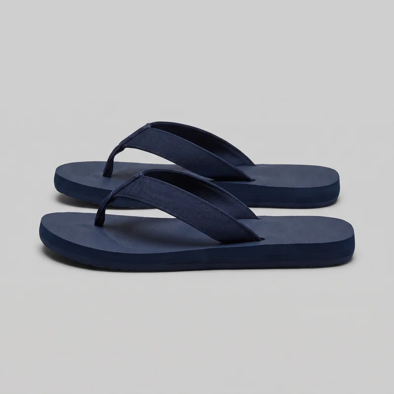 A complete pair of women's navy thong flip-flop sandals is shown as a standalone product, with the front sandal overlapping the rear one. Both sandals have open toes and heels, flat low-profile soles with rounded rectangular edges, and wide V-shaped straps anchored by central toe posts. The footbeds have lightly textured surfaces, with shallow tread visible along the bottom edge.