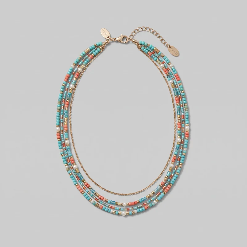 A complete multi-strand beaded necklace is laid out in an oval shape. Several parallel strands combine round and cylindrical beads in varied sizes with small spacer beads and occasional larger round accents, alongside a separate fine chain strand. The clasp, extension chain, end caps, jump-ring connectors, and oval dangling logo tags are visible near the top.