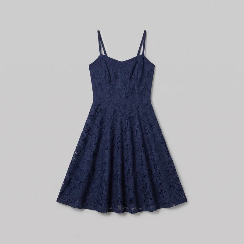 A complete standalone view of a navy women's sleeveless fit-and-flare dress with narrow adjustable spaghetti straps, an open-shoulder construction, and a shallow sweetheart neckline with a center dip. The fitted bodice has vertical shaping seams and joins the full A-line skirt at a defined waist seam. All-over floral openwork lace covers the dress, which ends in a gently curved, scalloped-looking lace hem.