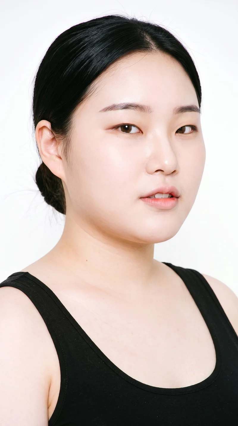 This 18-year-old Korean woman has a light porcelain skin tone with a cool undertone. Her heart-shaped face has a wider forehead that narrows to a more pointed chin. She has medium-thickness eyebrows, very dark near-black eyes, and thin lips. Her deep black hair is smoothed back into a neat low bun at the nape.