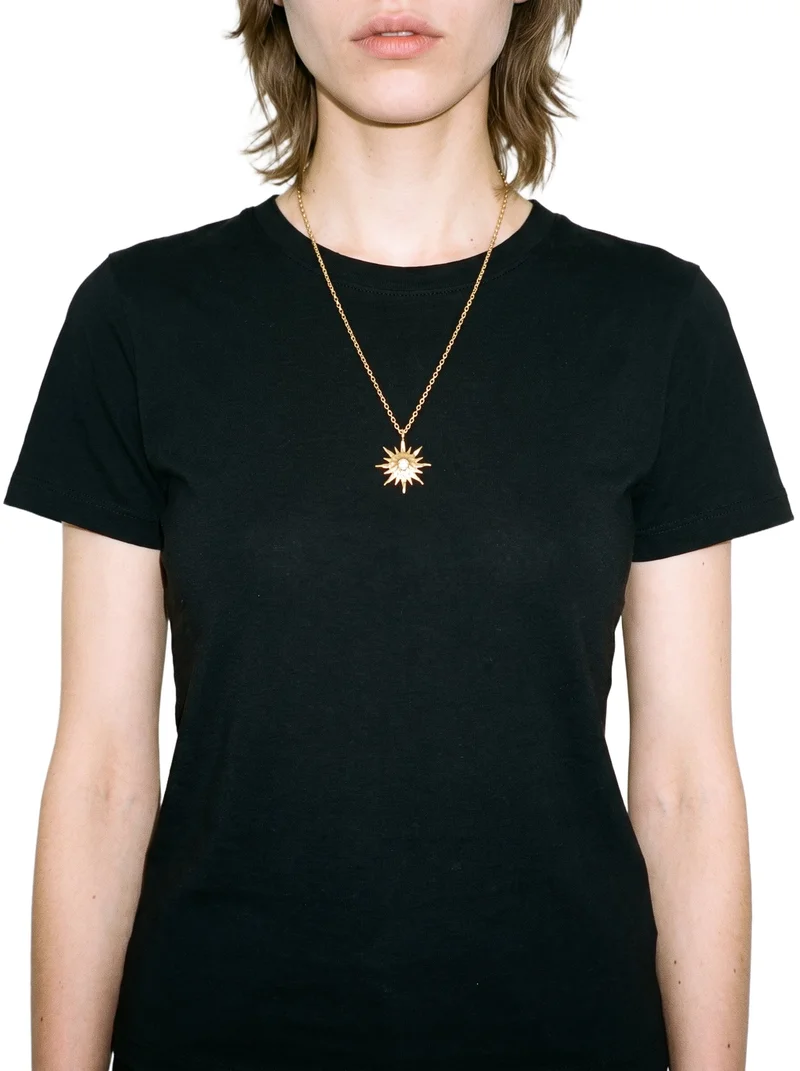 A woman wearing a gold pendant necklace is shown from the front in a torso-length view, with her arms relaxed. The necklace is displayed against a pure white backdrop.