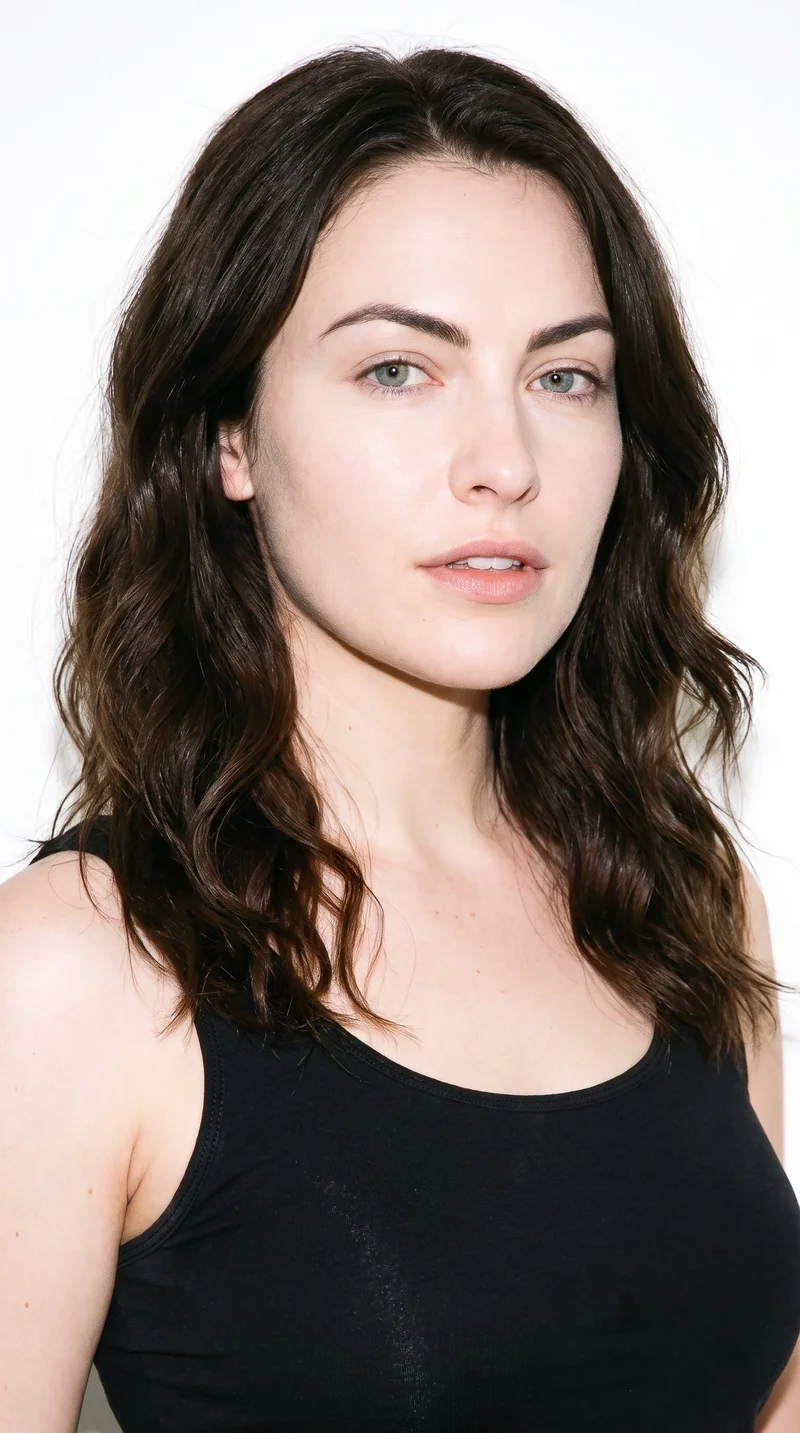 A 26-year-old Caucasian woman with fair skin and a cool undertone has an oval face with balanced proportions and a softly rounded jaw. Her medium-thickness eyebrows frame grey eyes with a cool, clear tone, and she has full lips. Her dark-brown hair falls in loose, slightly tousled waves with natural volume.
