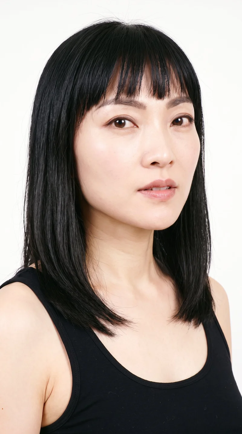 A 37-year-old Chinese woman with a light porcelain skin tone and cool undertone has a heart-shaped face, with a wider forehead narrowing to a more pointed chin. She has medium-thickness eyebrows, brown eyes, and thin lips. Her deep black hair falls across her forehead in bangs and frames the upper face.