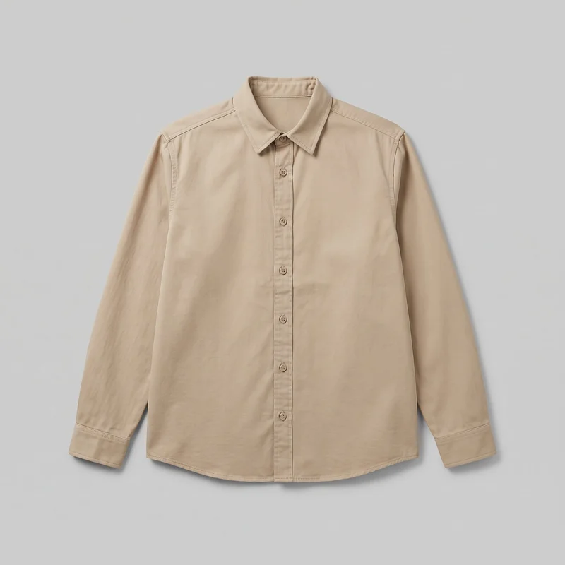 A beige twill overshirt is laid flat in a mostly complete front view. It has a pointed fold-down collar, full button placket, long set-in sleeves with banded cuffs, visible shoulder and sleeve seams, stitched placket and collar edges, and a gently curved shirttail hem. No chest pockets, logos, prints, patches, embroidery, or embellishments are visible.
