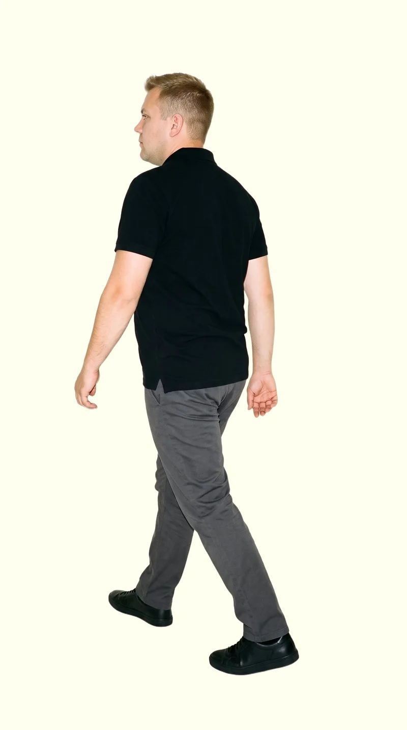 A 33-year-old Caucasian man wearing a black polo shirt is shown full body from an angled rear view while walking. An ivory lace backdrop surrounds the studio-cutout composition.