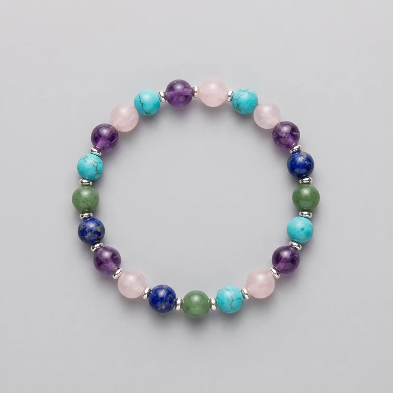 A complete women's gemstone beaded stretch bracelet is laid flat in an oval loop. The continuous circular strand combines uniformly round polished beads in varied translucent, opaque, marbled, veined, and speckled finishes with small shiny spacer rings placed singly or in pairs. No clasp, logo, print, embroidery, or other embellishment is visible.