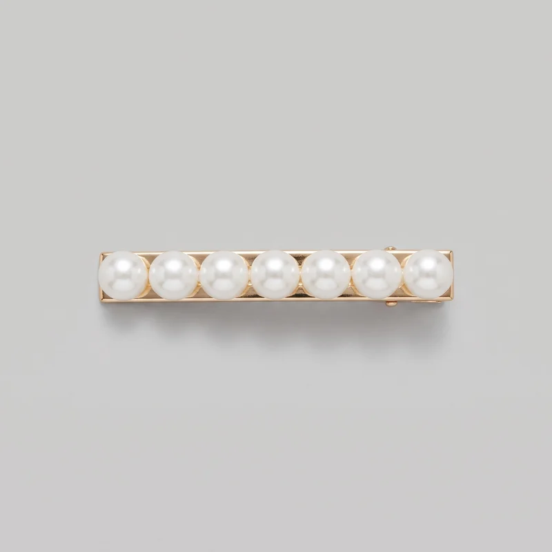 A complete Pearl Hair Clip is shown as a standalone bar-style barrette viewed from the front. It has a narrow elongated rectangular frame with raised rim edges, a single row of seven round domed beads across the front, and small clasp hardware visible behind the bar near both ends.