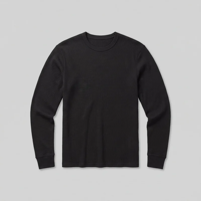 A complete flat front view shows a black men's long-sleeve thermal top with a regular straight silhouette, round bound crewneck, set-in sleeves, wide smooth cuffs, and a straight bottom hem. The shirt has an all-over raised waffle-knit texture with plain neck and cuff binding, subtle shoulder and armhole seams, and no visible pockets, closures, logos, or embellishments.