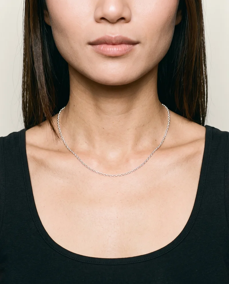 A silver chain necklace is shown from the front on a straight neck, framed closely around the neck against an Oyster Pearl studio-wall backdrop.