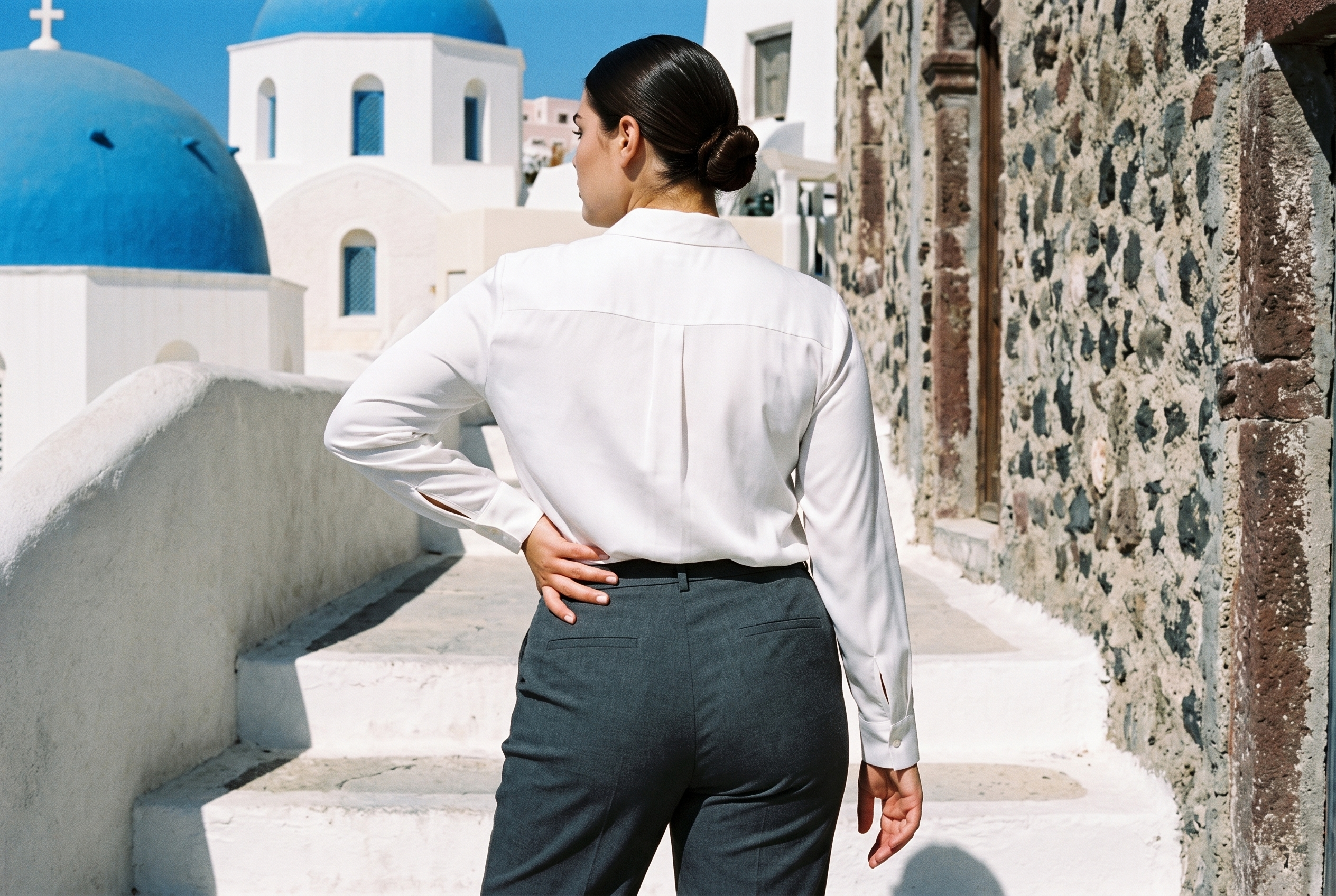 A 23-year-old Caucasian woman wears a white silk blouse in a three-quarter-length back view, with her weight positioned toward the back. White steps form the backdrop.