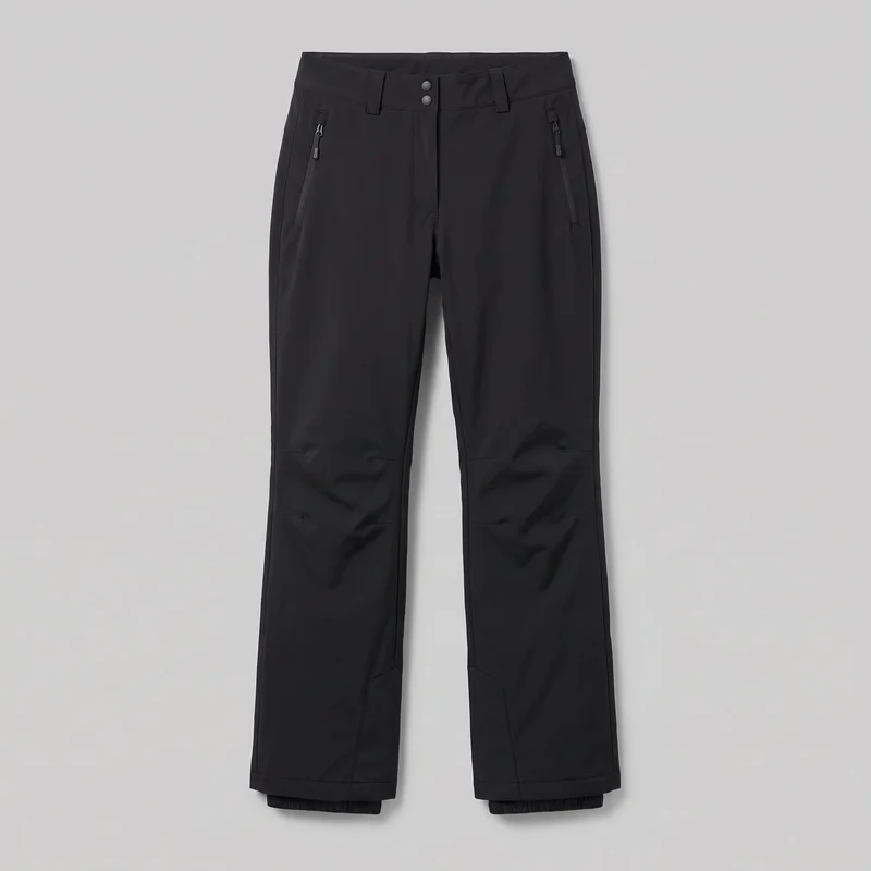 Women's black technical ski trousers laid flat in a full front view. They have a mid-rise waistband with belt loops, a centered fly with two round fasteners, vertical zip pockets at the hips, articulated knee seams, lower-leg panel seams, and slightly widened boot-compatible hems with inner elastic gaiter cuffs visible below.