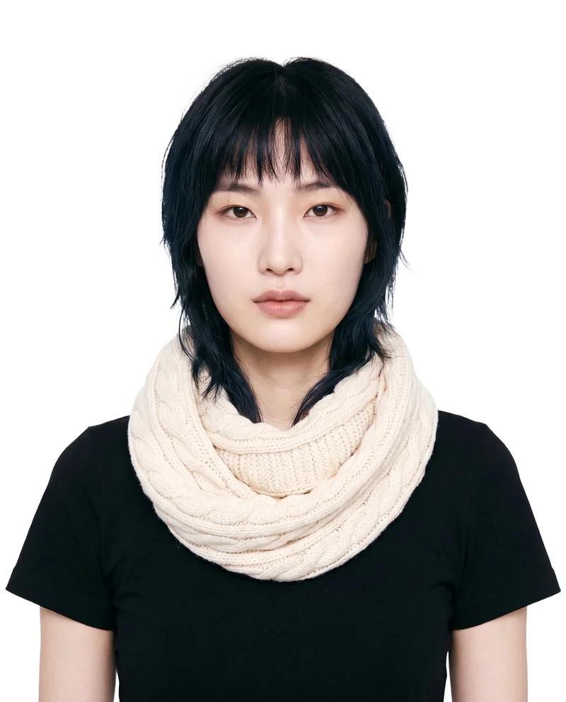 A 27-year-old Korean woman wears a cream cable-knit snood in a front-facing bust composition. Her head is level and her expression is neutral, against a pure white backdrop.