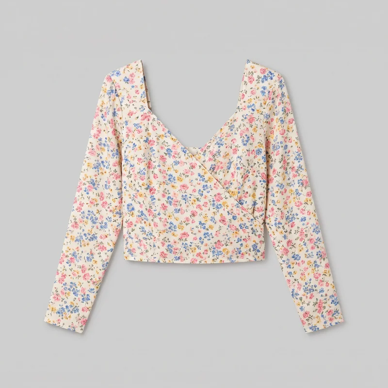 A women's cropped wrap blouse is laid flat in a front view. It has a deep V neckline formed by overlapping crossover panels, a straight cropped hem, long sleeves with volume through the arms, and visible gathering and soft pleating at the shoulders. The blouse is covered in a small floral print of scattered blossoms and leaves.