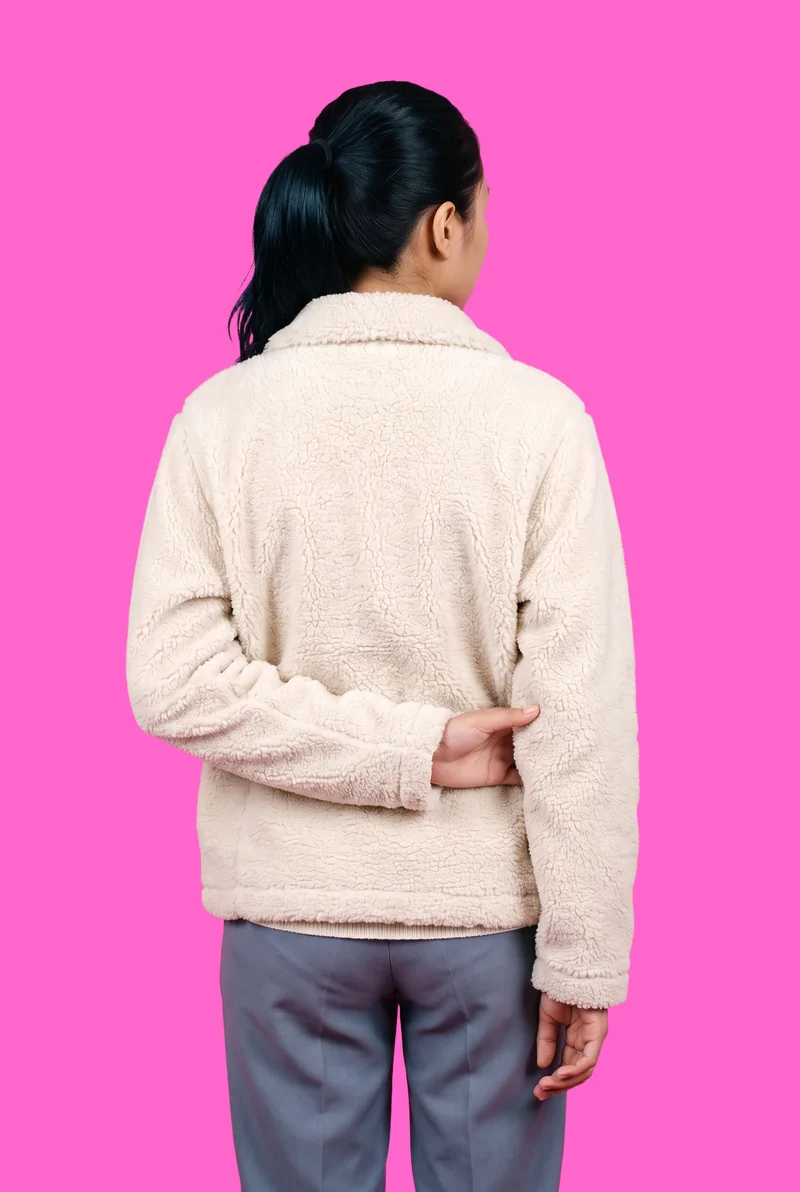 A 21-year-old Southeast Asian woman wears a cream sherpa fleece jacket in a three-quarter-length back view, with one elbow positioned behind her back. A flat rose-pink backdrop fills the background.